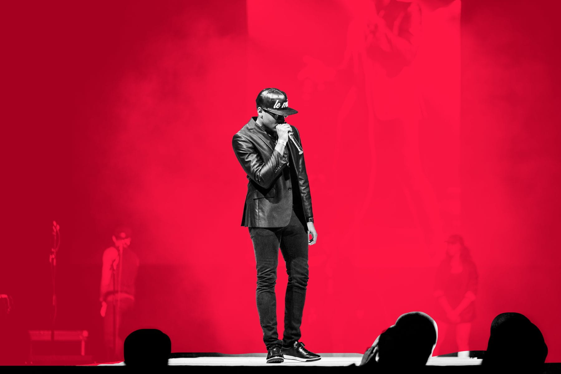 Ace Anderson performing under red light, mic in hand, silhouettes in the foreground